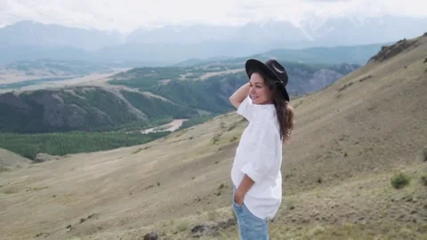 Attractive brunette in a hat and white shirt is enjoying nature in the mountains Видео 131281988