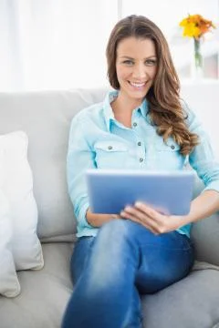 Attractive brunette sitting on couch using tablet Stock Photos
