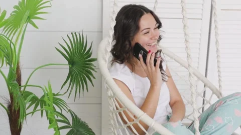 Attractive brunette talking on the phone while sitting on a swing at home. woman 库存影片 131595724