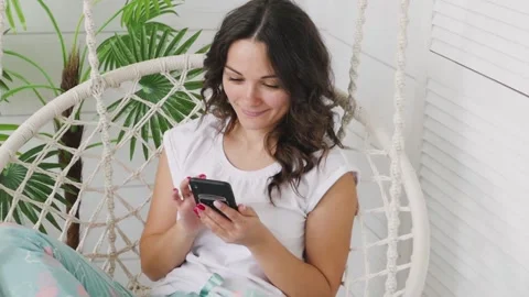 Attractive brunette talking on the phone while sitting on a swing at home. woman Stock-Footage 131597297