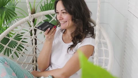 Attractive brunette talking on the phone while sitting on a swing at home. woman 库存影片 131597480