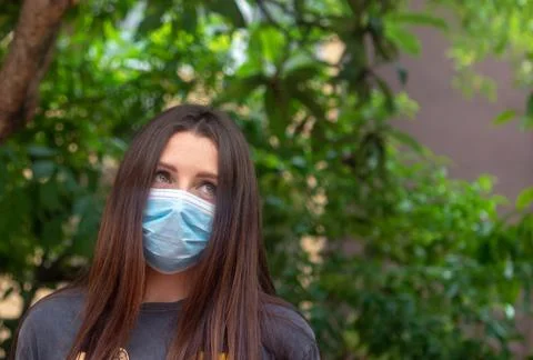 Attractive brunette wearing a light blue surgical mask looking into the dista Stock Photos