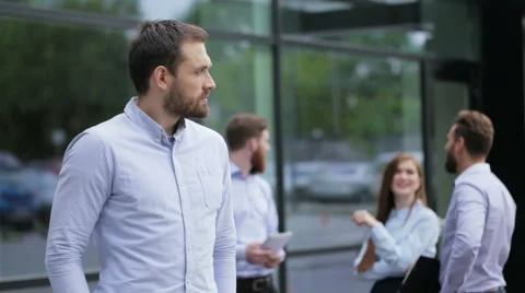 Attractive businessman posing on a camera , his colleagues talking to each Stock Footage 64110264