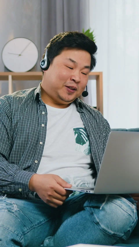Attractive cheerful young asian guy in headset enjoying his video call while sit Stock Footage 325626313