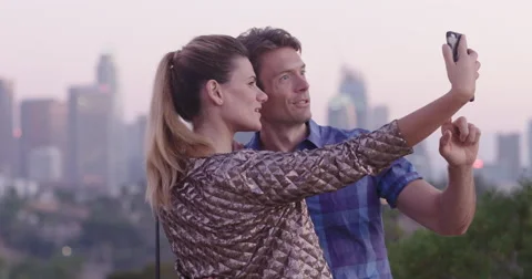 Attractive couple pull faces for cellphone photos in front of LA skyline 4K Stock Footage 68182636