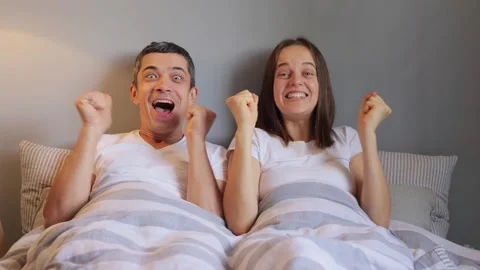 Attractive couple reclining in comfortable bed delightfully watching movie Stock Footage 252831140