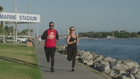 Attractive couple runs down path at Marina Park in SLOW MOTION Vídeos de archivo 136022565
