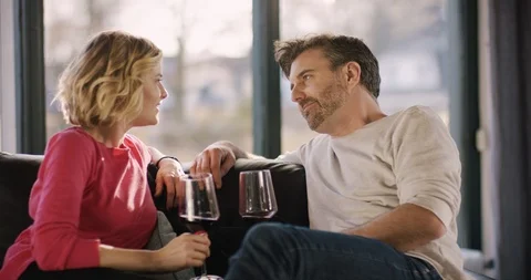 Attractive Couple sitting on couch; clinking glasses; smiling at each other Stock Footage 86294990