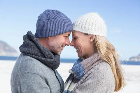 Attractive couple smiling at each other on the beach in warm clothing Stock Photos