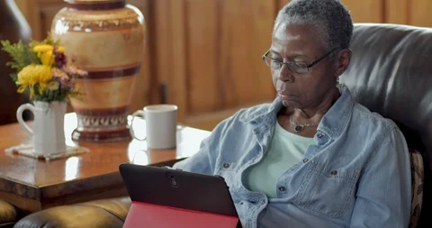 Attractive elderly black woman using a digital tablet in her living room - dolly Stock Footage