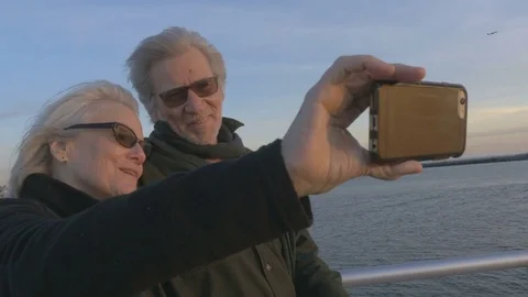 Attractive elderly couple in 60s take selfie on ocean with smartphone at sunset Stock Footage 74434039