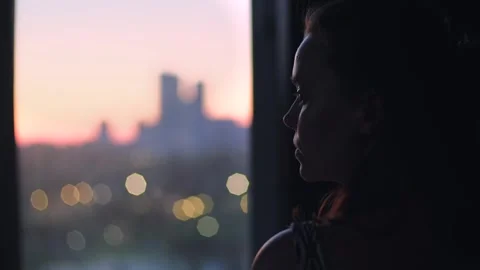 Attractive female watching sunset over cityscape through window. Portrait of Stock Footage 253181453