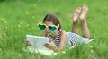 Attractive girl in big sunglasses with tablet computer lies on green grass HD Footage
