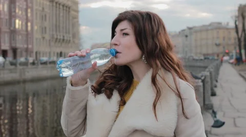 Attractive girl drinks water from a plastic bottle in the old city centre near Stock-Footage 62430053