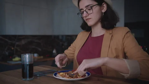 An attractive girl eats a slice of pizza while sitting at a table wearing a hat Stock Footage 314522019