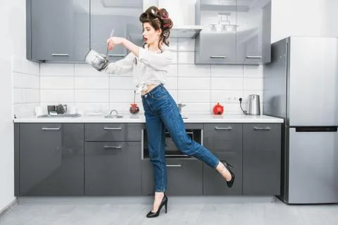 An attractive girl in everyday clothes and curlers is cooking in the kitchen. Stock Photos