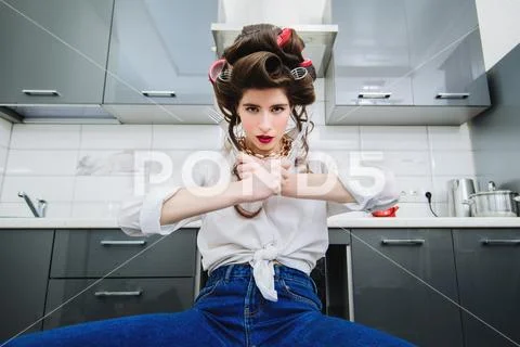 An attractive girl in everyday clothes and curlers is ready for the meal in t Stock Photos