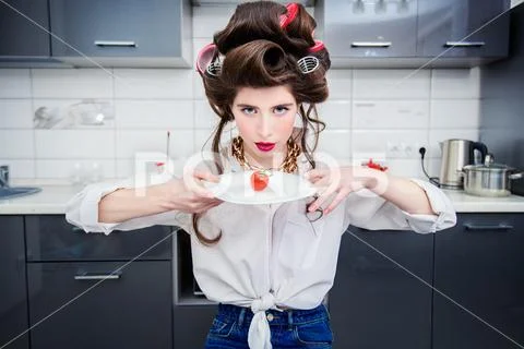 An attractive girl in everyday clothes and curlers is tasting a dish in the k Stock Photos