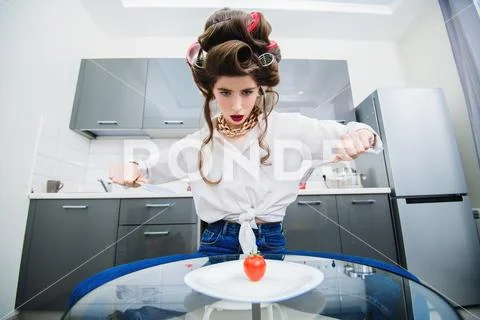 An attractive girl in everyday clothes and curlers is tasting a dish in the k Stock Photos