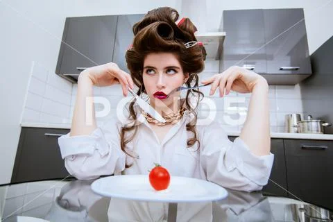 An attractive girl in everyday clothes and curlers is tasting a dish in the k Stock Photos