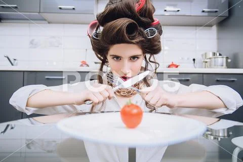 An attractive girl in everyday clothes and curlers is tasting a dish in the k Stock Photos