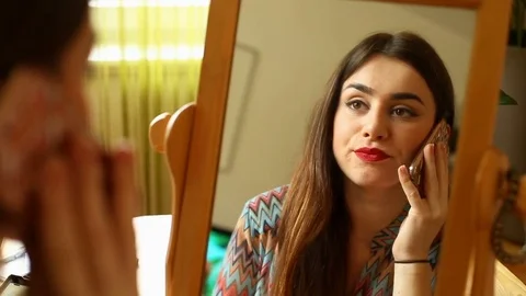 Attractive girl looking on her reflection in the mirror and talking on cellphone Stock Footage 73684253