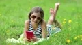 Attractive girl in sunglasses with red smartphone lies on the grass HD Footage