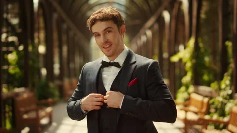 Attractive groom posing under arch in garden. Man buttoning up jacket in park Video stock 141293826