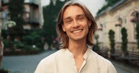 An attractive guy with a beard and long hair in a light shirt stands outside and Stock Footage 127068741