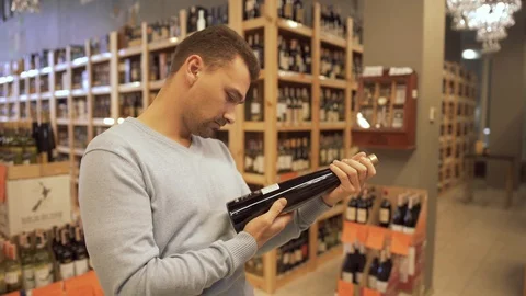 Attractive guy carefully examines the composition on the label of a wine bottle Video stock 99385023