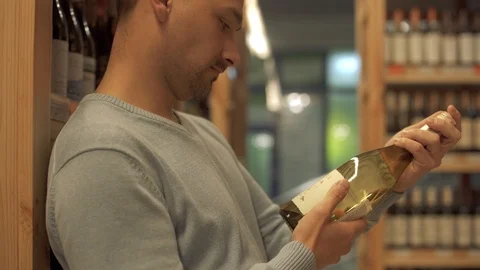 Attractive guy carefully examines the composition on the label of a white wine Video stock 99386166