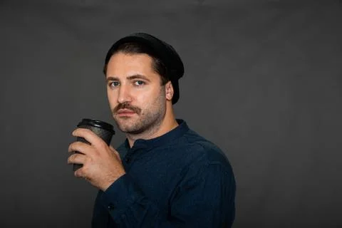Attractive guy looks at camera while drinking coffee on dark background, relax Stock Photos