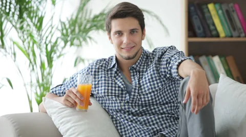 Attractive guy sitting on couch drinking juice and smiling Video stock 28791195