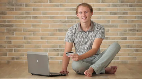 Attractive guy sitting on floor using laptop holding credit card and smiling  Vídeos de archivo 34278115