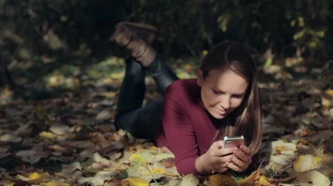 Attractive happy female student using smart phone at autumn park. Stock Footage 68982230
