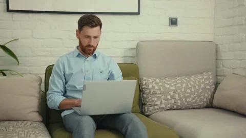 Attractive happy man using laptop sitting on couch in modern living room at home Stock Footage 132539543