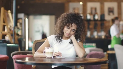 Attractive hispanic girl using smartphone and smiles in a coffee house. Stock Footage 88290696