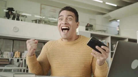 Attractive hispanic the guy plays a game on the phone and wins, rejoices in Stock Footage 152938986