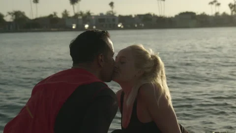 Attractive interracial couple share a romantic kiss at sunset by the water Stock Footage 136033946