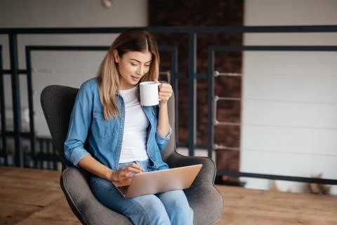 Attractive lady smiling while using her laptop and drinking coffee Stock Photos