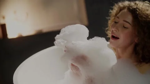 An attractive lady spends her evening taking a bath with foam. A curly-haired Stock Footage 239633714