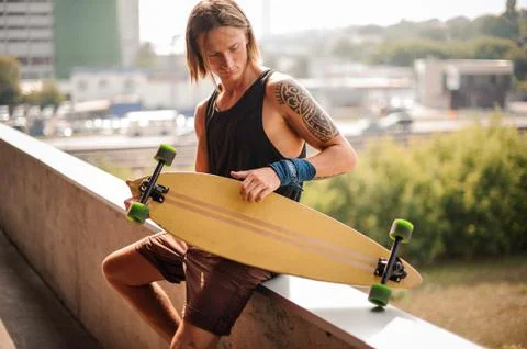 Attractive long-haired guy sitting on the parapet with longboard 库存照片