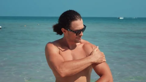 Attractive man applying sunscreen while relaxing beach. Sunscreen is evenly Stock Footage 312741424