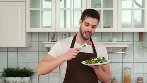 An attractive Man in an apron tastes a cooked vegan salad and enjoys it. Stock Footage 151403473