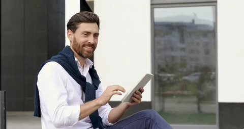 Attractive man with beard greeting someone with hand while sitting outdoors with Stock Footage 140680940