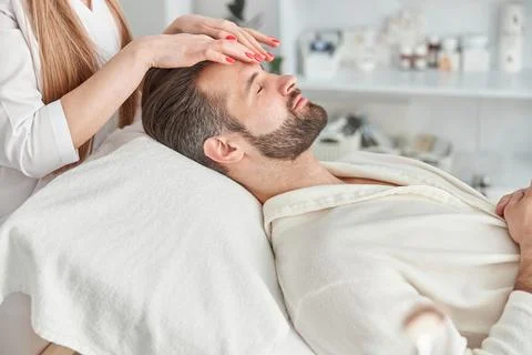 Attractive man with beard is lying on back, getting face lifting massage. Facial Stock Photos