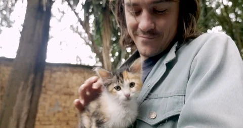 Attractive man being affectionate to a tiny young kitten he's holding Video stock 80816538