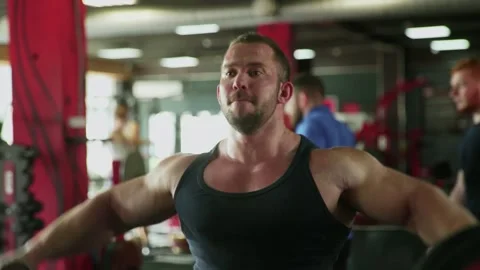 An attractive man bodybuilder performing Side raise exercise with dumbbells at Stock Footage 143521421