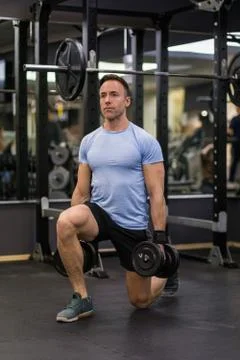Attractive man doing lunges step-ups with heavy dumbbell. Stock Photos