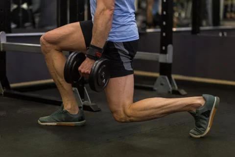 Attractive man doing lunges step-ups with heavy dumbbell. Stock Photos